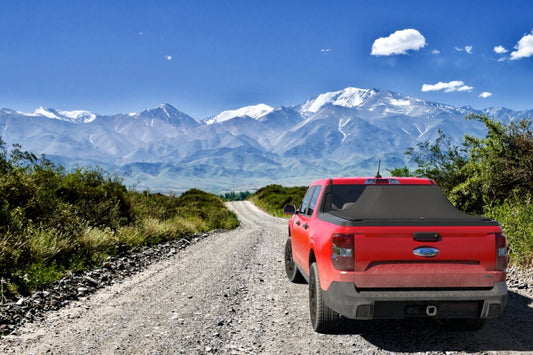 Red Ford Maverick on a gravel road with mountains in teh background carrying a loaded Sawtooth Truck bed cover