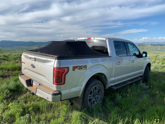 Silver Ford F-150 With a Sawtooth STRETCH tonneau cover covering a large loadin a field with light blue sky