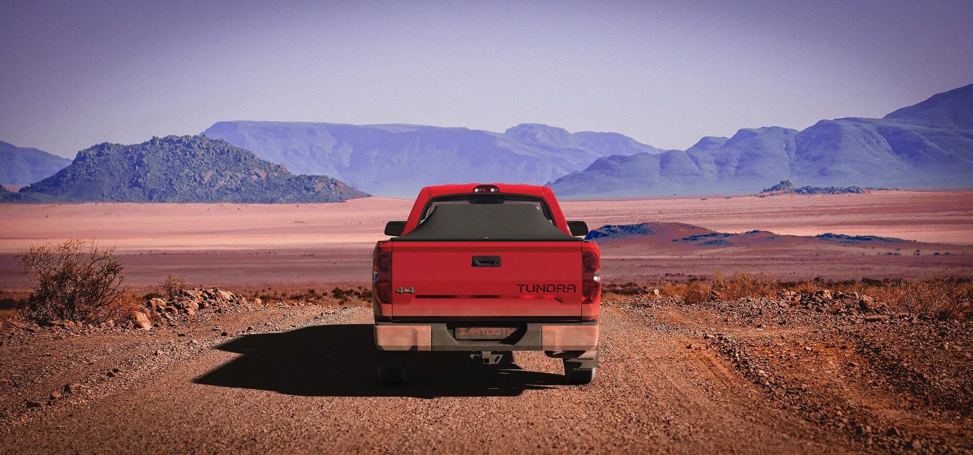 Red Toyota Tundra with an expanded Sawtooth Tonneau by a road with mountains in the background