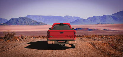 Red Toyota Tundra with an expanded Sawtooth Tonneau by a road with mountains in the background