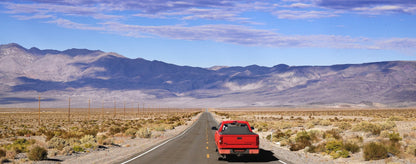 Red Toyota Tundra with an expanded Sawtooth Tonneau by a road with mountains in the background