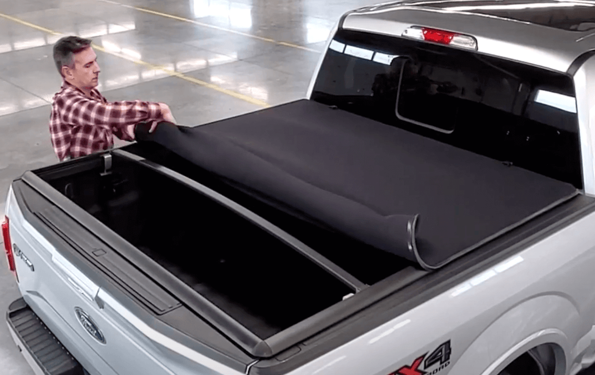 Man installing a black tonneau cover on a white Ford truck bed.