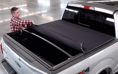 Man installing a black tonneau cover on a white Ford truck bed.