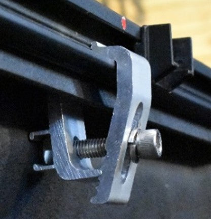 Close-up of a metal mounting bracket with a threaded bolt and adjustment screw, attached to a black rail or frame for a Sawtooth STRETCH truck bed cover.