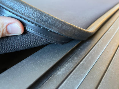 Close-up of a person's finger lifting the corner of Sawtooth A.C.M.S. aluminum frame J-hook against a ribbed dark surface.