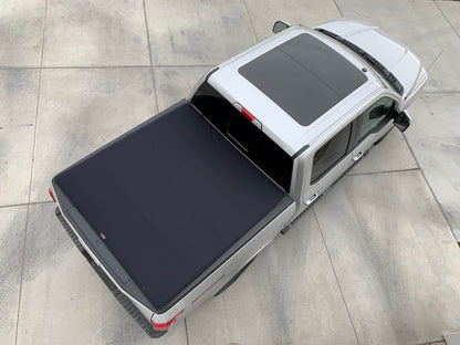 A silver pickup truck shown from a high-angle overhead view, fitted with a dark Sawtooth Expandable tonneau cover on the bed, parked on a light gray concrete surface.