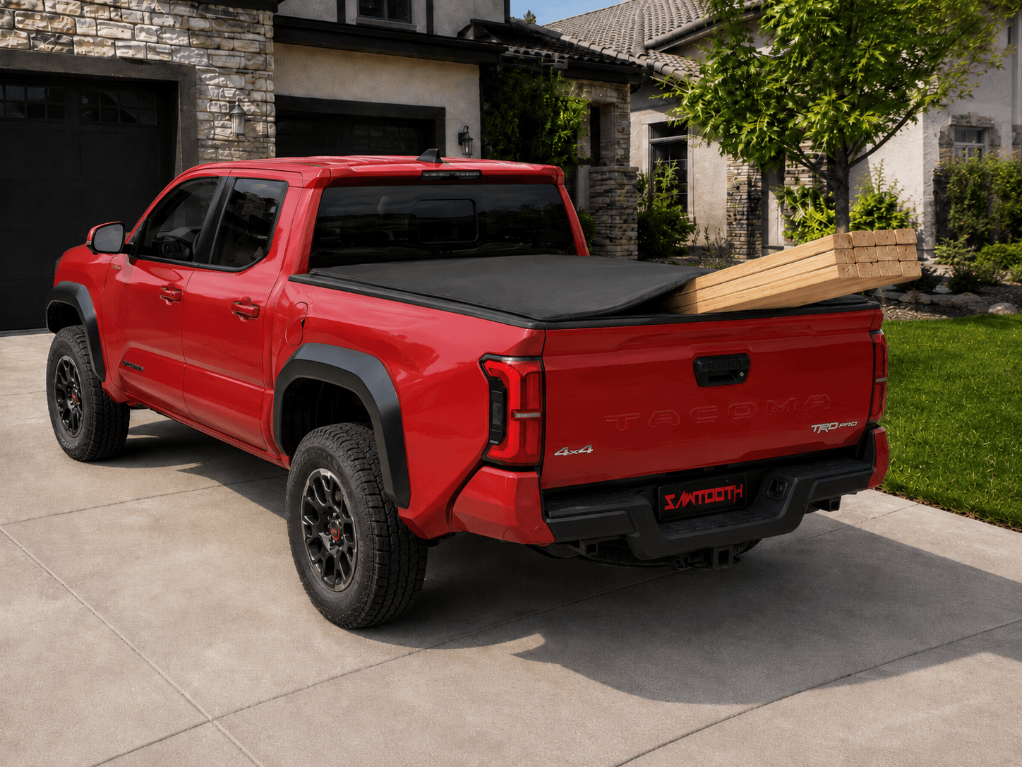 A red pickup truck parked on a concrete driveway in front of a suburban house. The truck is shown from a rear three-quarter angle, featuring a black tonneau cover on the bed, black wheels, and a black rear bumper with a visible XPTOOTH logo.