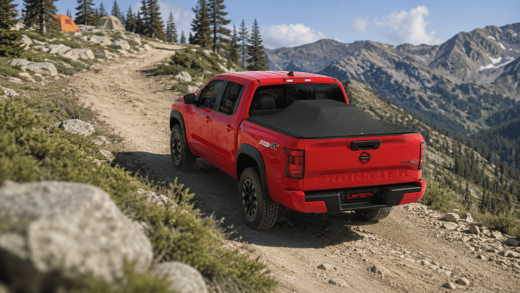 A red Nissan Quads Lite pickup truck with a black tonneau cover drives along a dirt mountain road, with rocky terrain, pine trees, and rugged peaks in the background.