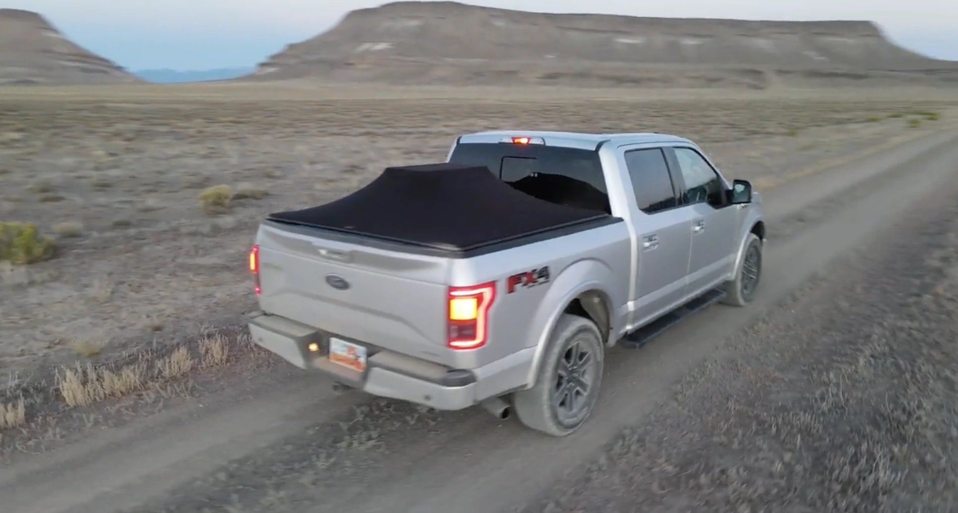 Truck bed cover installed on silver Ford pickup in rugged terrain

