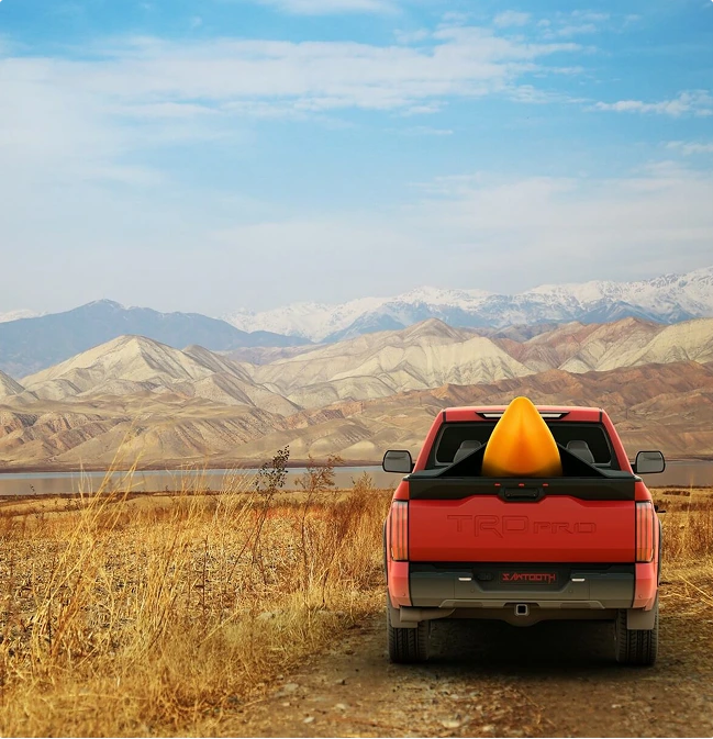 Red pickup truck carrying an orange cargo cone in a mountain desert landscape