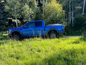Blue 2021 Ford Raptor 5' 7" Bed with Sawtooth Stretch tonneau expanded over short cargo load in the forest
